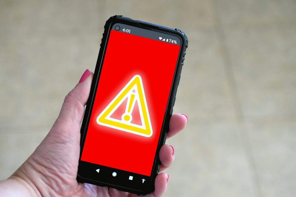 Phone screen showing red screen with yellow glowing danger sign. Concept hack virus cyber attack